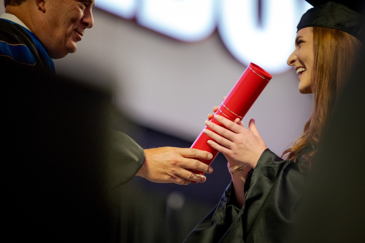 A graduate in her cap and gown receives a diploma from Terry College Dean Benjamin Ayers.