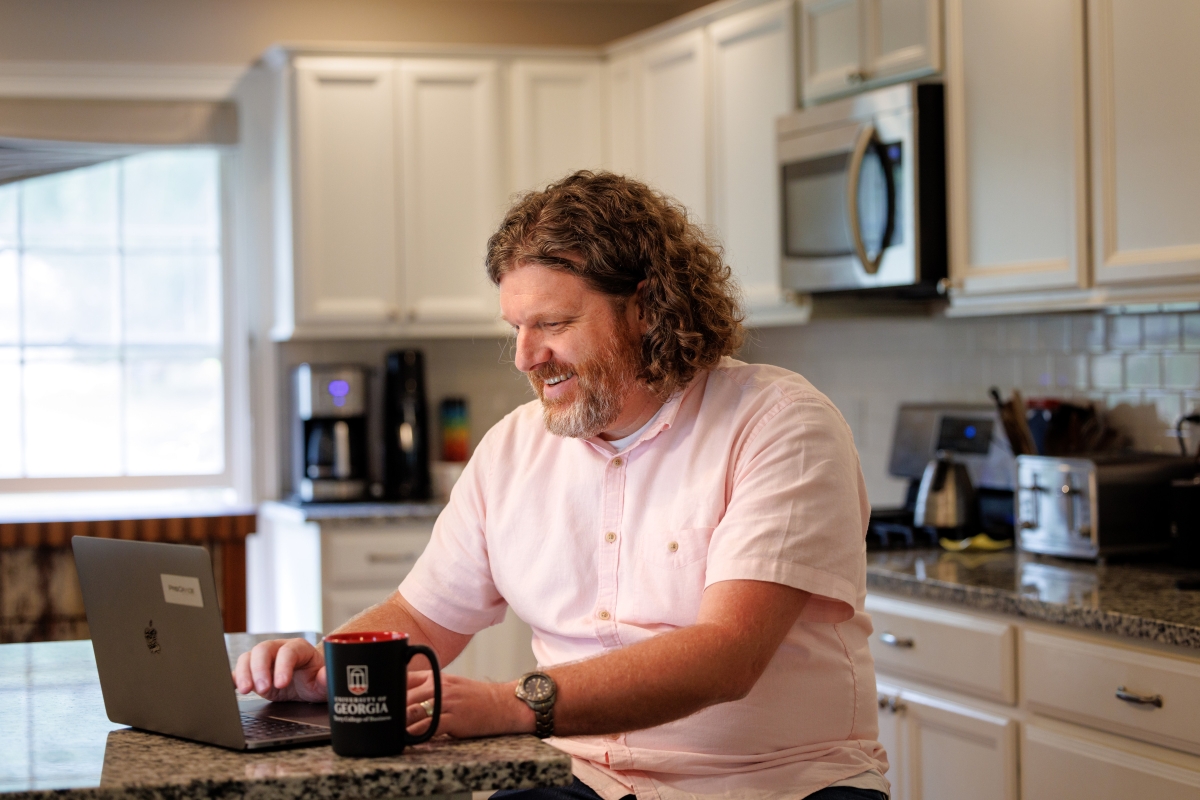 A man sits at kitchen counter, studying on his laptop.