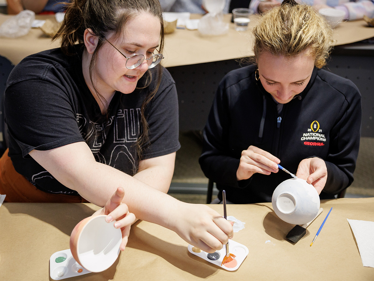 Hannah Potter, left, and Elsa Wust paint laugh together as they pain bowls.