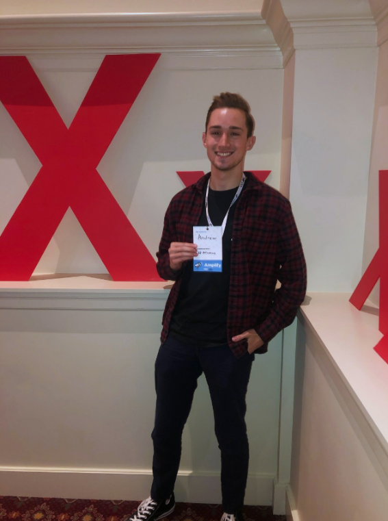 Andrew stands and holds his name badge