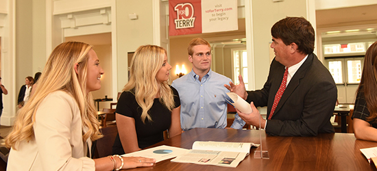 Three students stand at a table in the Casey Commons discussing success with a professional mentor