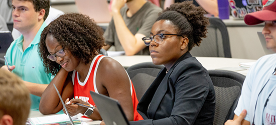 Two female students listen and take notes during a lecture