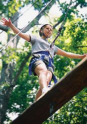 Student in a harness balances on thin beam at the ropes course