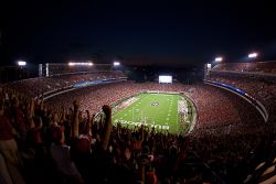 Sanford Stadium at night with field glowing and fans' hands raised cheering