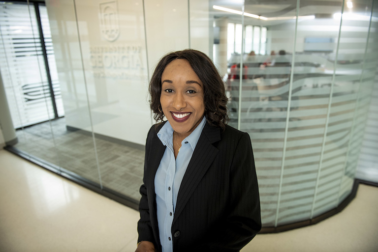 Professional woman stands in a business setting smiling at the camera with a look of success