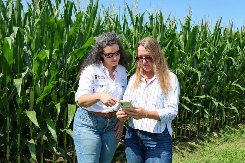 UGA Student Industry Fellow Bradley Smith, right, speaks with Lauren Lazaro, assistant professor and UGA Extension precision agriculture specialist, in front of a field of corn.