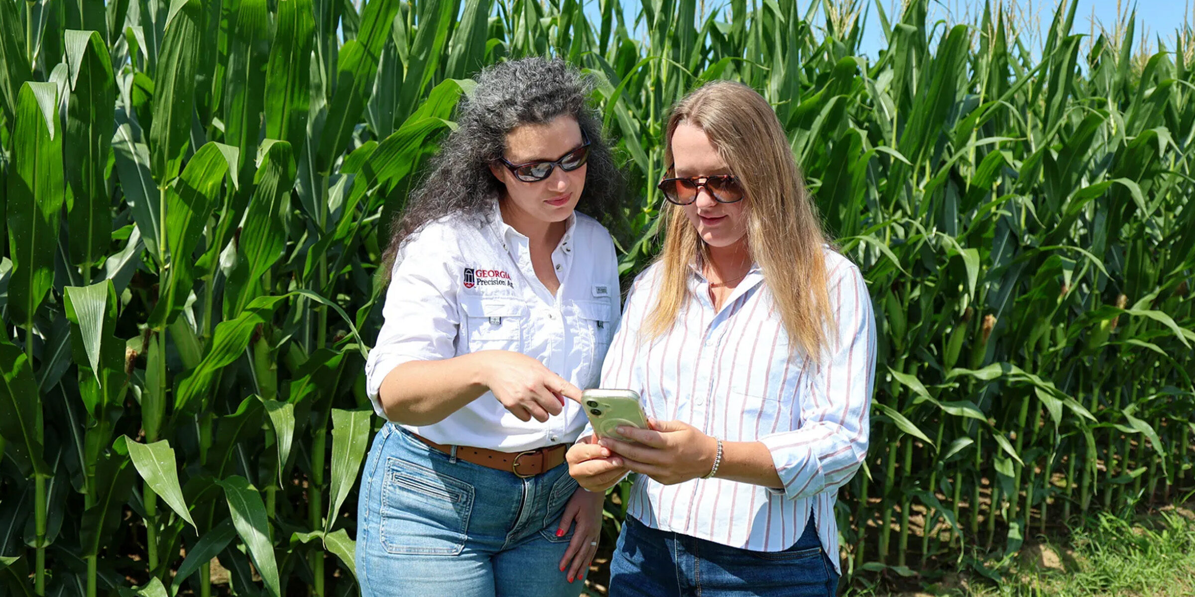 UGA Student Industry Fellow Bradley Smith, right, speaks with Lauren Lazaro, assistant professor and UGA Extension precision agriculture specialist, in front of a field of corn.