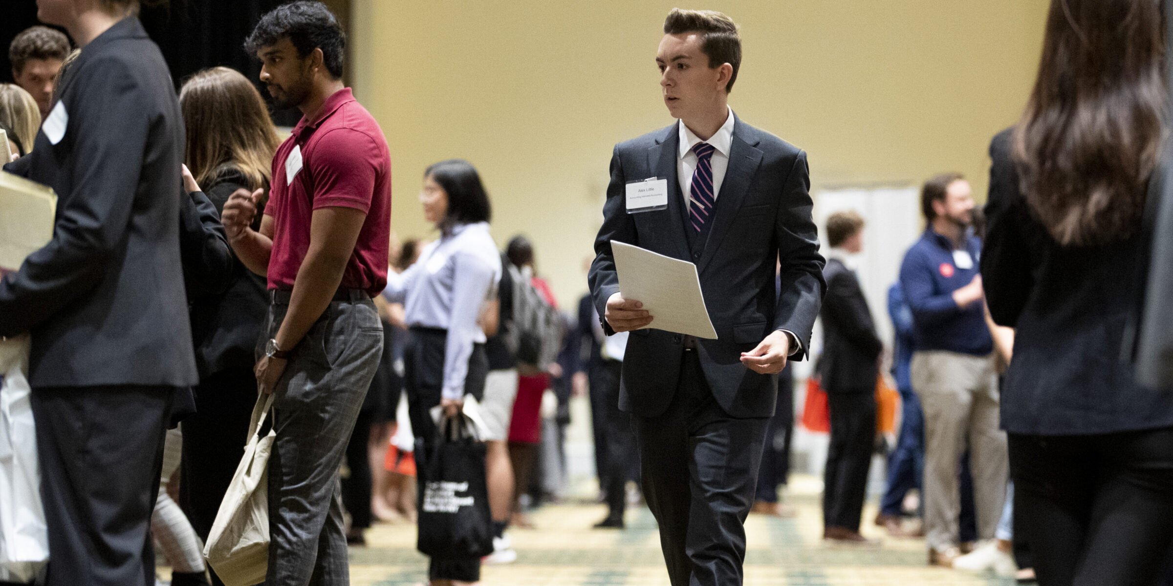 Student walking at career fair in a suit.