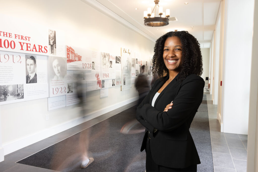 Kendall Valdry stands in a hallway in front of a Terry College of Business centennial timeline wall display at the UGA Business Learning Community