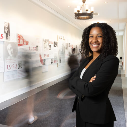 Kendall Valdry stands in a hallway in front of a Terry College of Business centennial timeline wall display at the UGA Business Learning Community