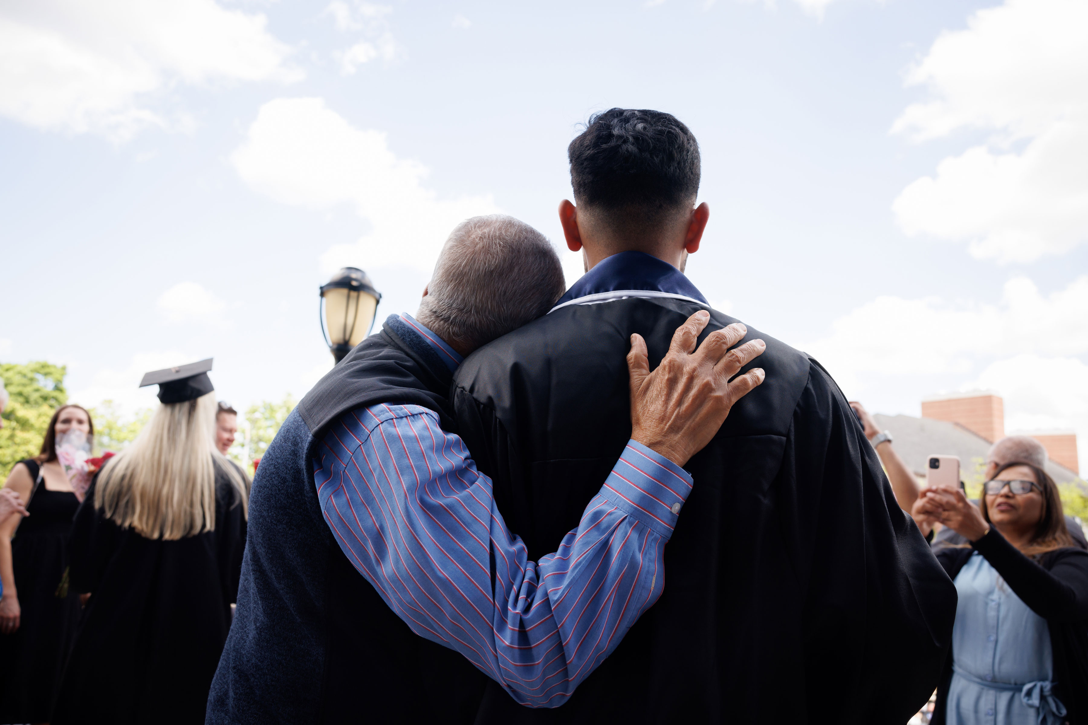 candid shot of father hugging son from back after convocation ceremony