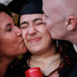 man and woman kissing female graduate in regalia