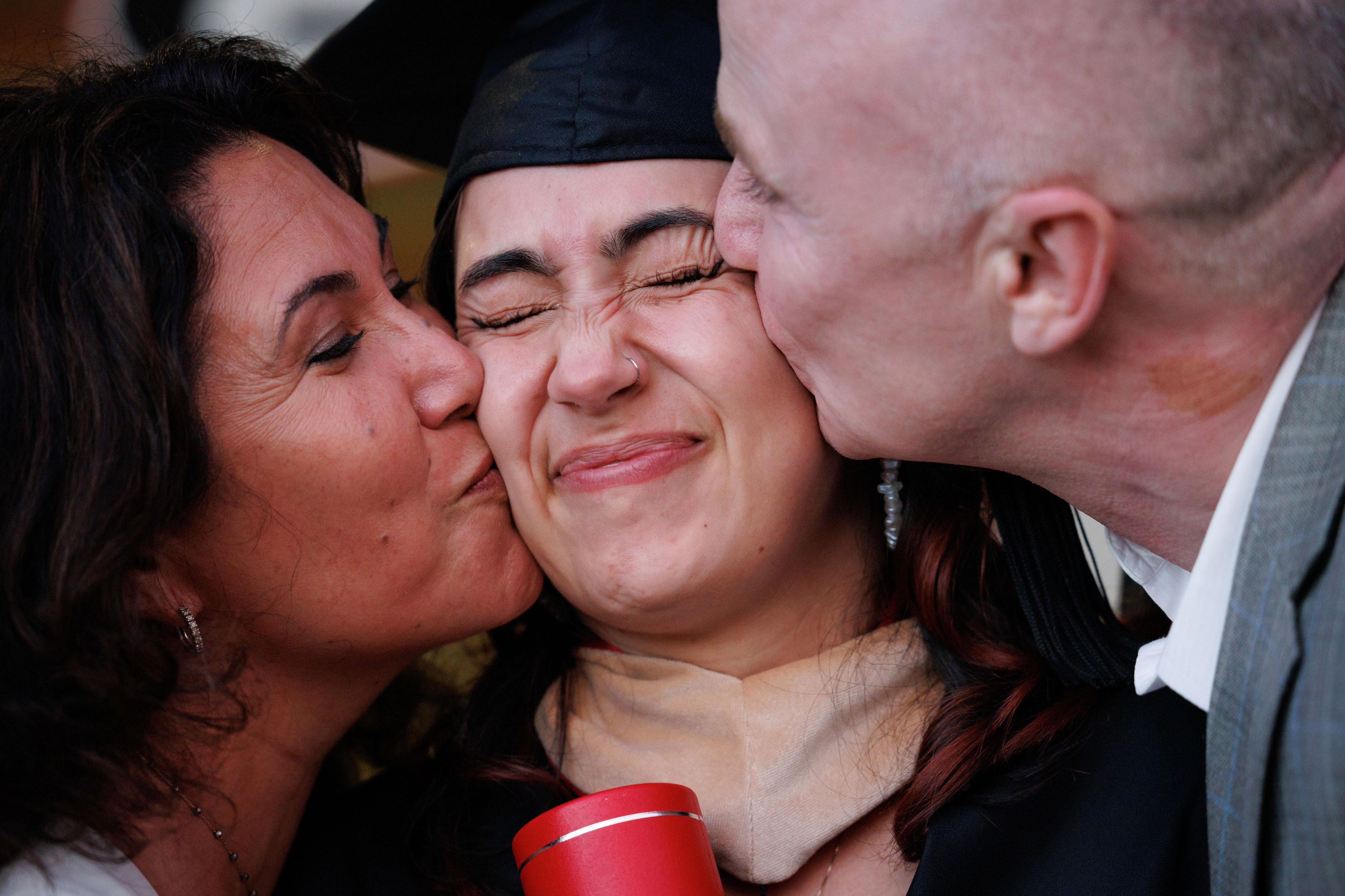 man and woman kissing female graduate in regalia