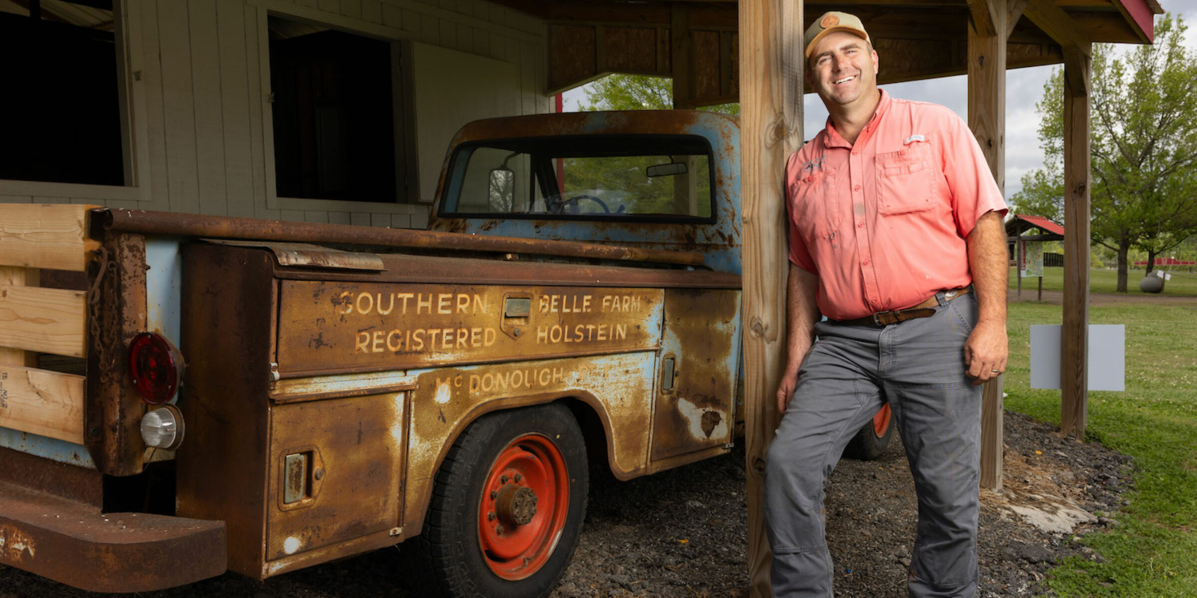 man leans against wooden beam next to vintage pickup truck