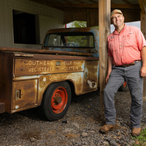 man leans against wooden beam next to vintage pickup truck