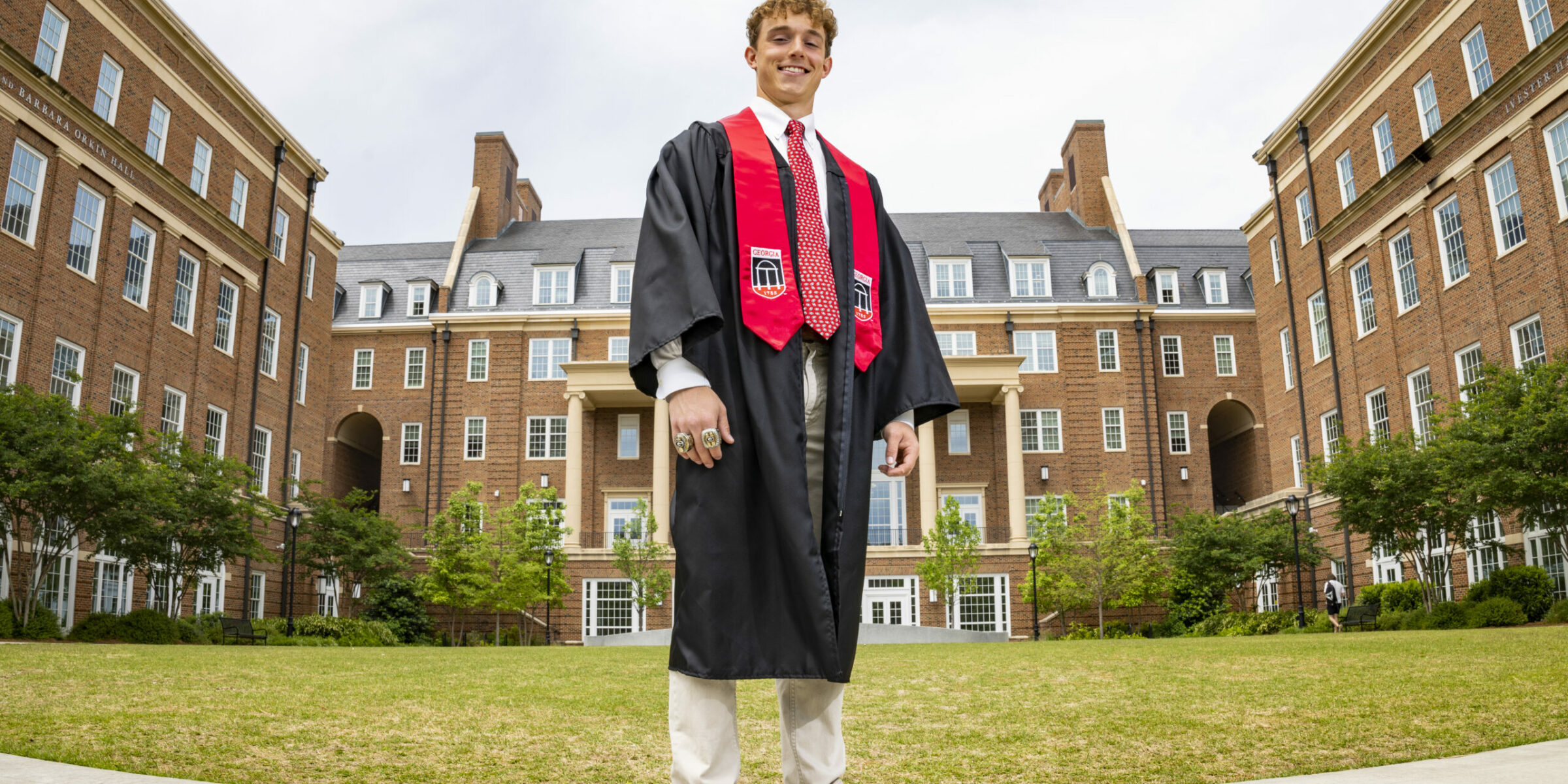 male student dressed in graduation regalia with brick buildings in background