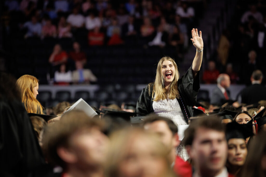 female waves to audience among sea of graduates