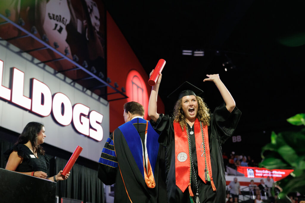 female graduate raises hands in celebration as she crosses stage
