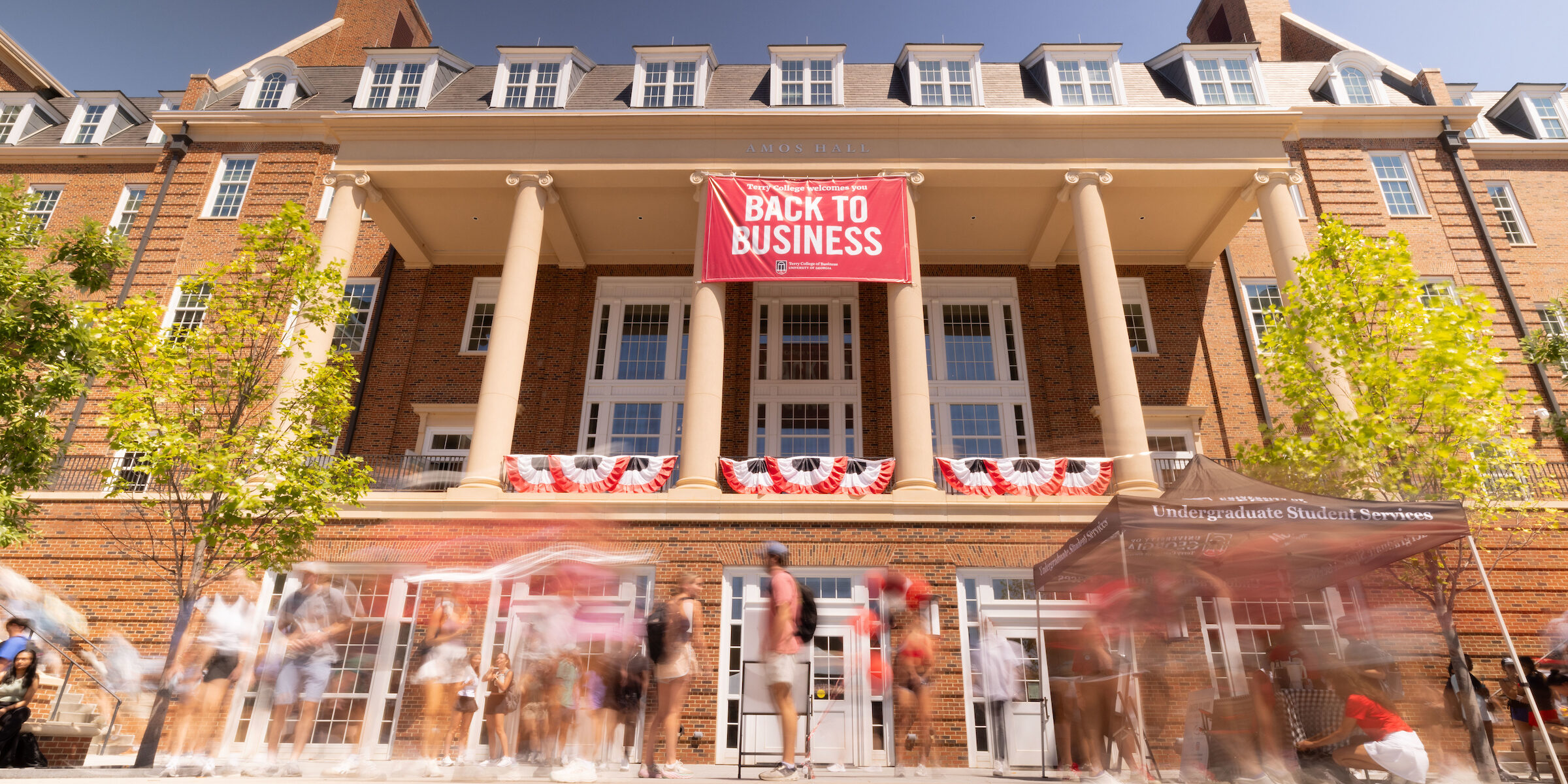 A crowd of people gather in Coca-Cola Plaza in front of a large "Back to Business' sign hung off of Amos Hall.