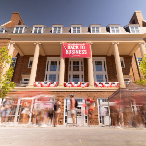 A crowd of people gather in Coca-Cola Plaza in front of a large "Back to Business' sign hung off of Amos Hall.