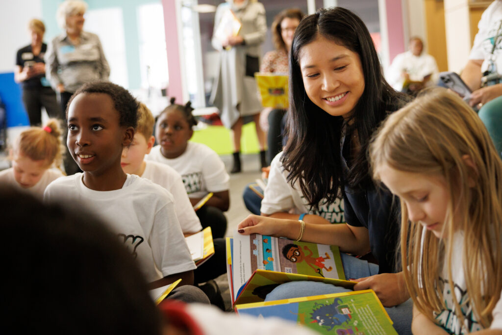 A Terry College volunteer sits with students on the floor of an elementary school library during storytime