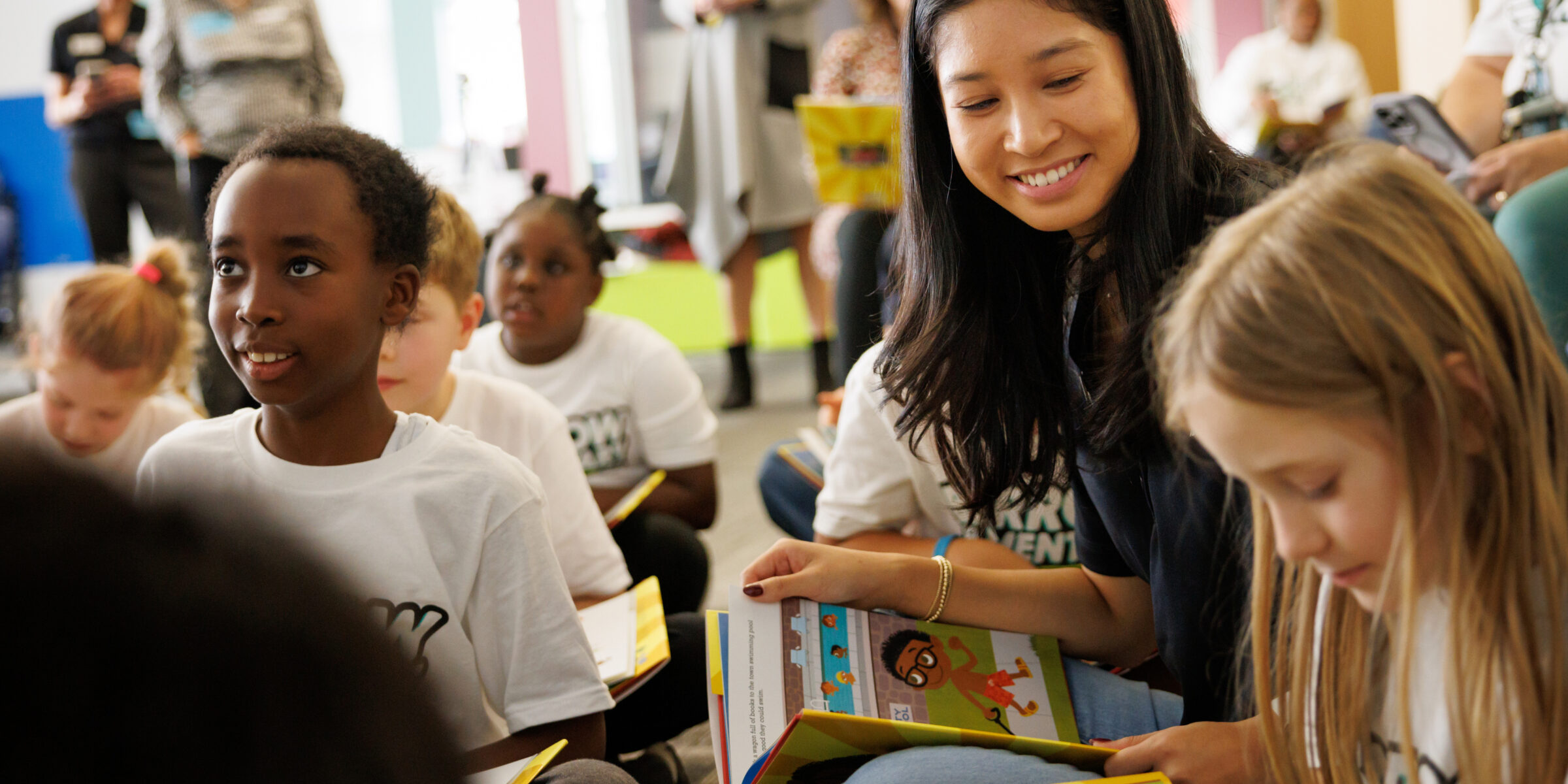 A Terry College volunteer sits with students on the floor of an elementary school library during storytime
