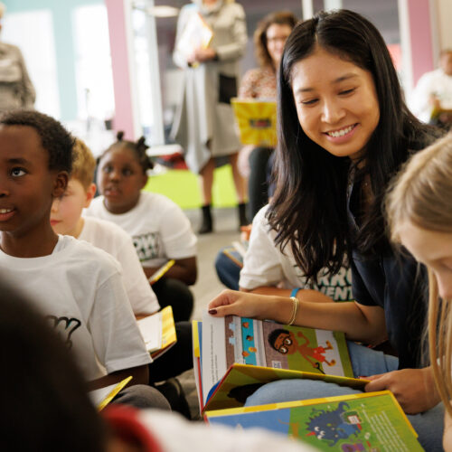 A Terry College volunteer sits with students on the floor of an elementary school library during storytime