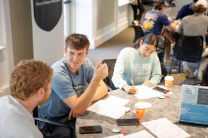Two men chat at a table while a woman studies