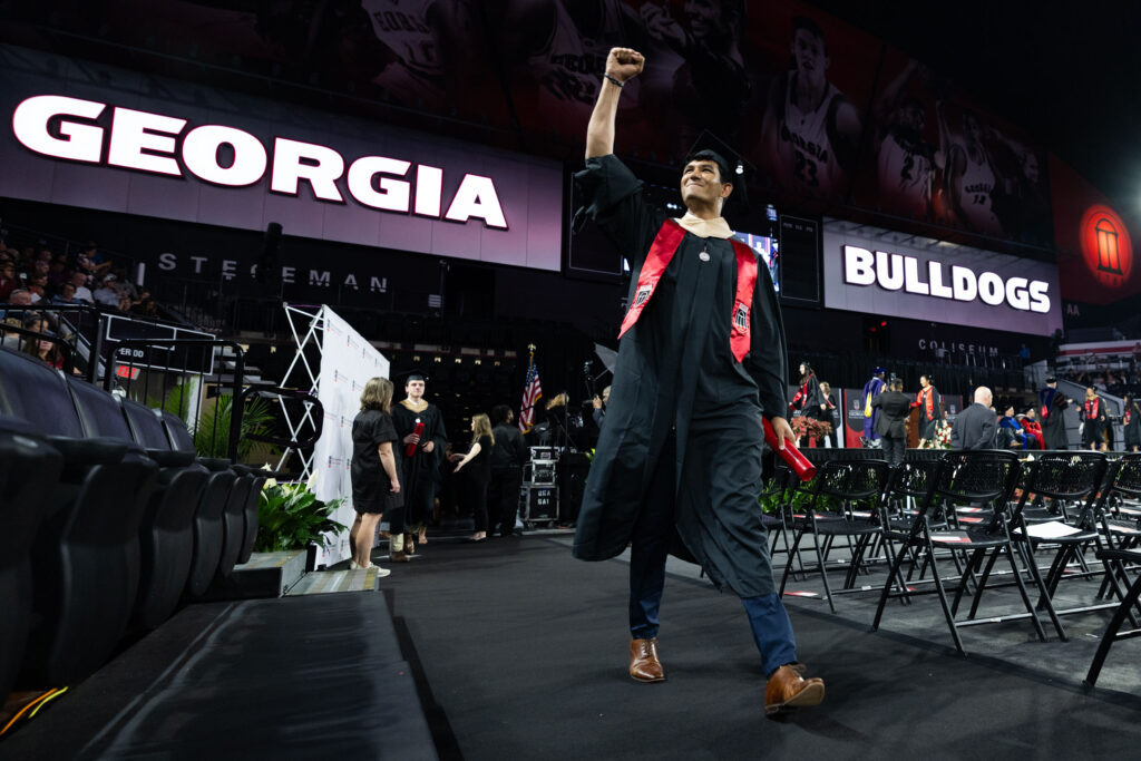 2026.05.07_rh_Grad_Convocation_007 A male graduate holds his fist up in celebration after walking across the stage at Stegman Coliseum at the 2026 Terry College of Business Graduate Convocation.