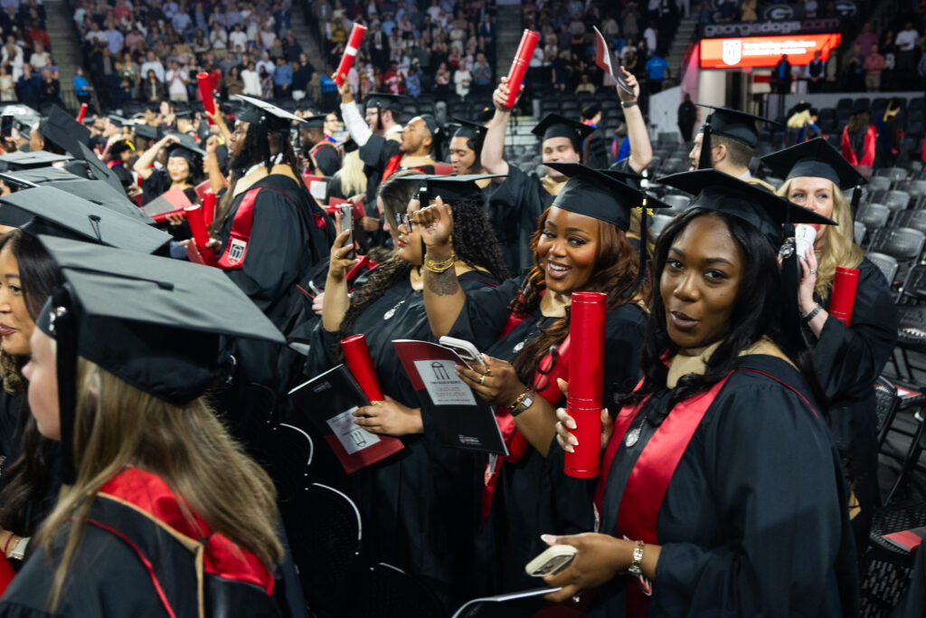 2026.05.07_rh_Grad_Convocation_008 Female graduates celebrate in their row on the floor of Stegman Coliseum at 2026 Terry College of Business Graduate Convocation