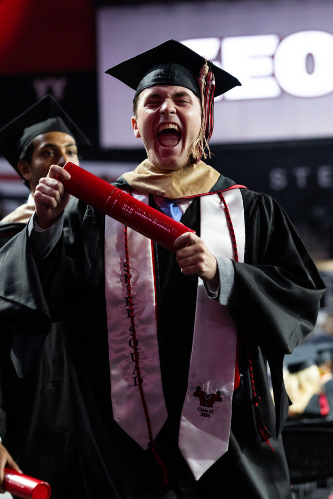 2026.05.07_rh_Grad_Convocation_013 A male graduate holds his diploma tube and yells in celebration in at the 2026 Terry College of Business Graduate Convocation