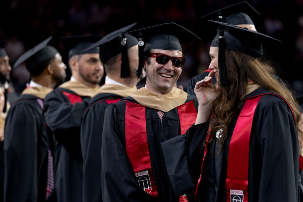 Graduates chat while waiting to walk across the stage at Stegman Coliseum the 2026 Terry College of Business Graduate Convocation.