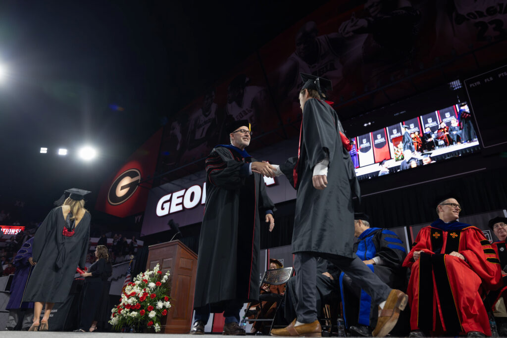 2026.05.07_rh_Grad_Convocation_044 MBA director Jason Mathews shakes the hand of a graduate on stage during UGA Terry College of Business attend their convocation ceremony at Stegman Coliseum.
