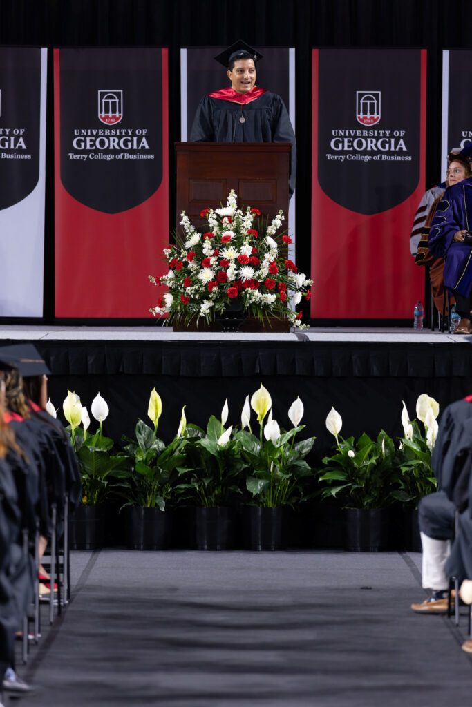 2026.05.08_rh_Undergrad_Convocation_028 Terry alumnus Paul Shoukry speaks from a podium on stage at Stegeman Coliseum while a crowd of graduates watches during Terry College Undergraduate Convocation on May 8.