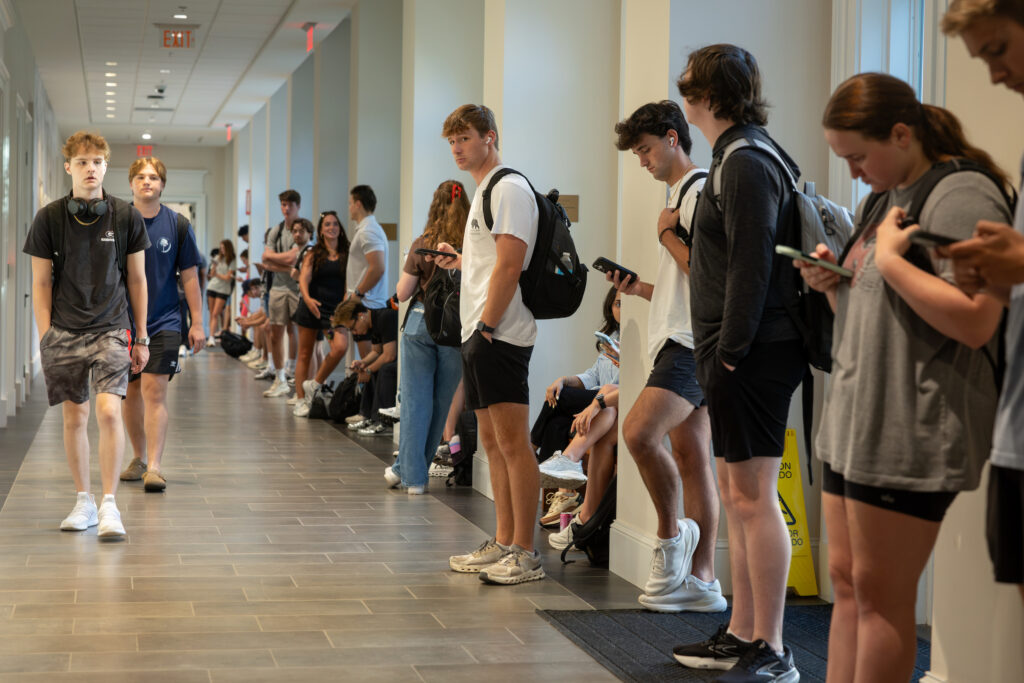 University of Georgia fall semester begins University of Georgia fall semester beginsA line of young people waits in a hallway, many looking at their phones, while two individuals walk past them.University of Georgia fall semester begins