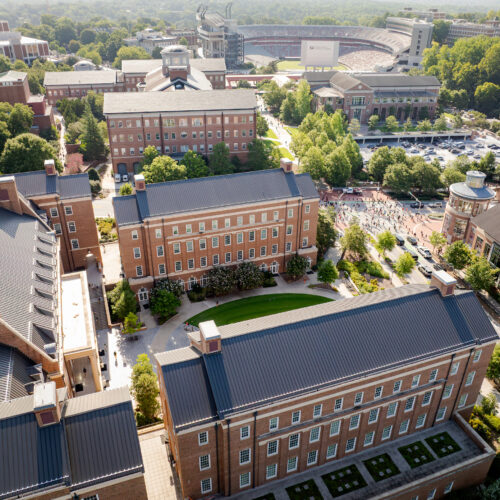 An aerial view of a university campus featuring brick buildings, green lawns, and a large stadium surrounded by trees.