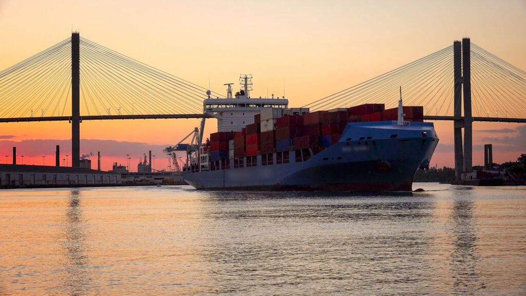 A container ship navigates through a port during sunset.