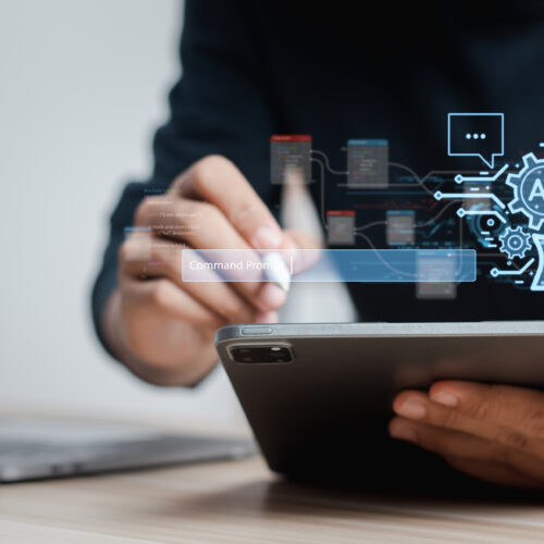 A close up of man's hand as we works on a tablet computer with a stylus. An illustration of a a head and a gear with the initials AI centered hovers superimposed above his tablet. How to budget for AI innovation?