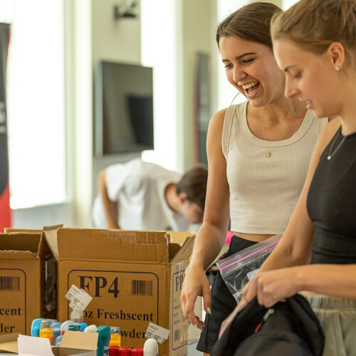 Two female students chat while packing backpacks at the B.A.G.