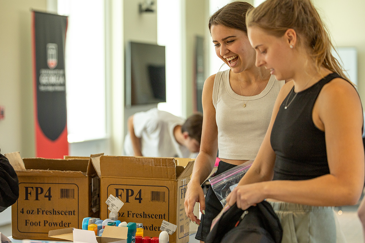 Two female students chat while packing backpacks at the B.A.G.