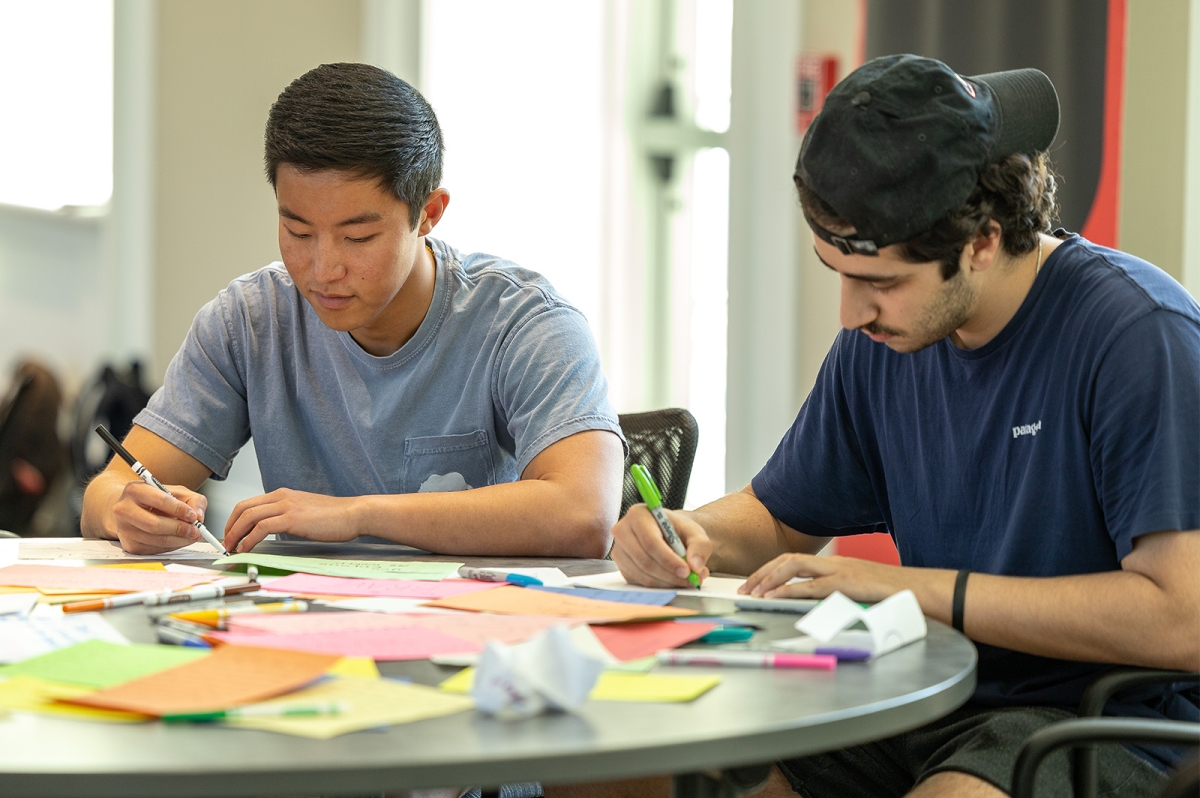 Two students writing notes to pack in backpacks for homeless people