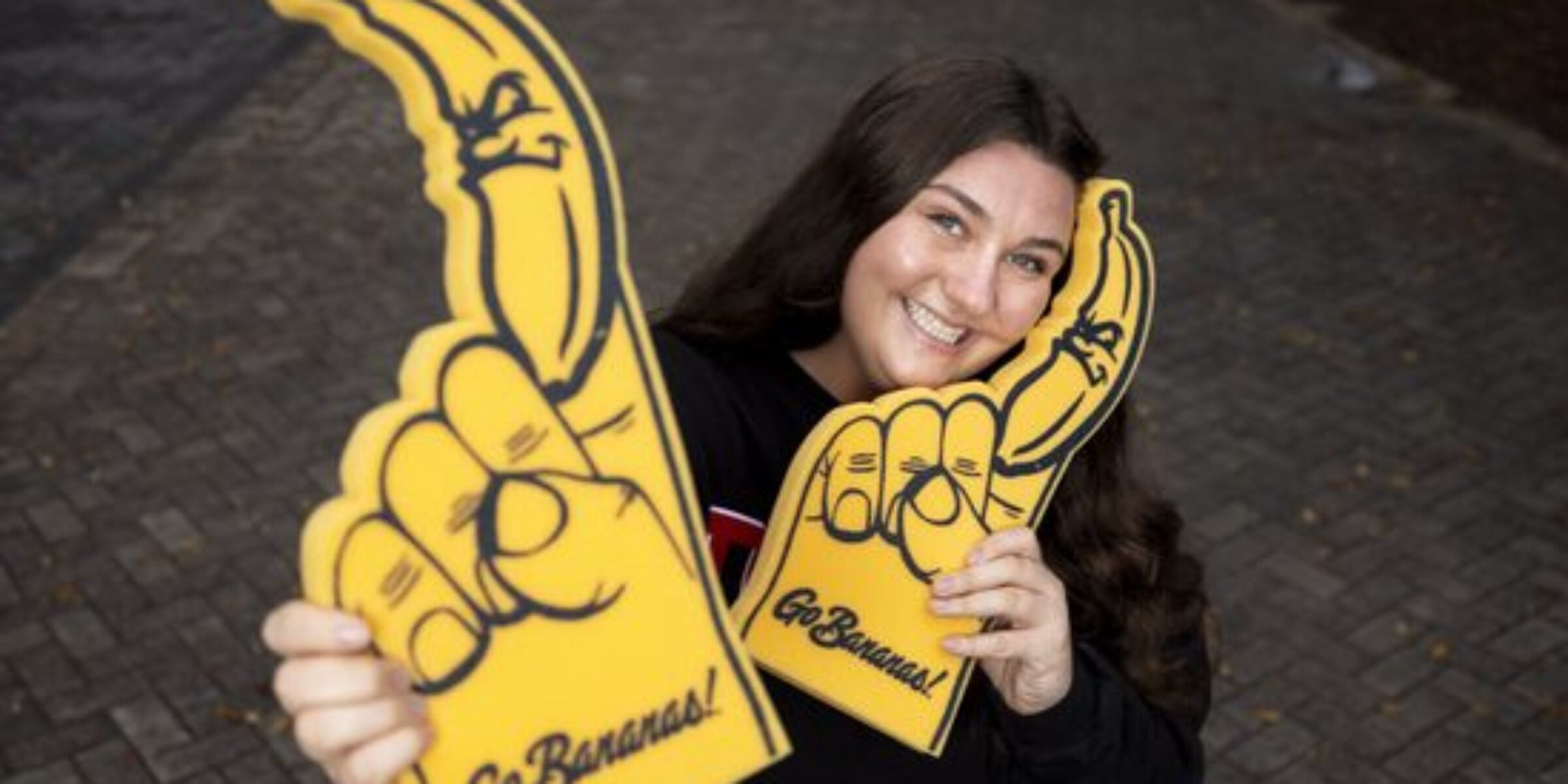 Maren Finnegan a young woman poses with two Savannah Bananas foam fingers.