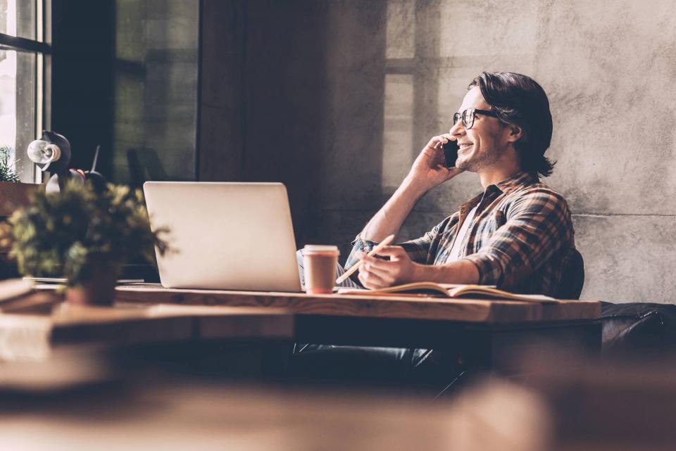 Casual gentleman sits at his laptop while talking on the phone.