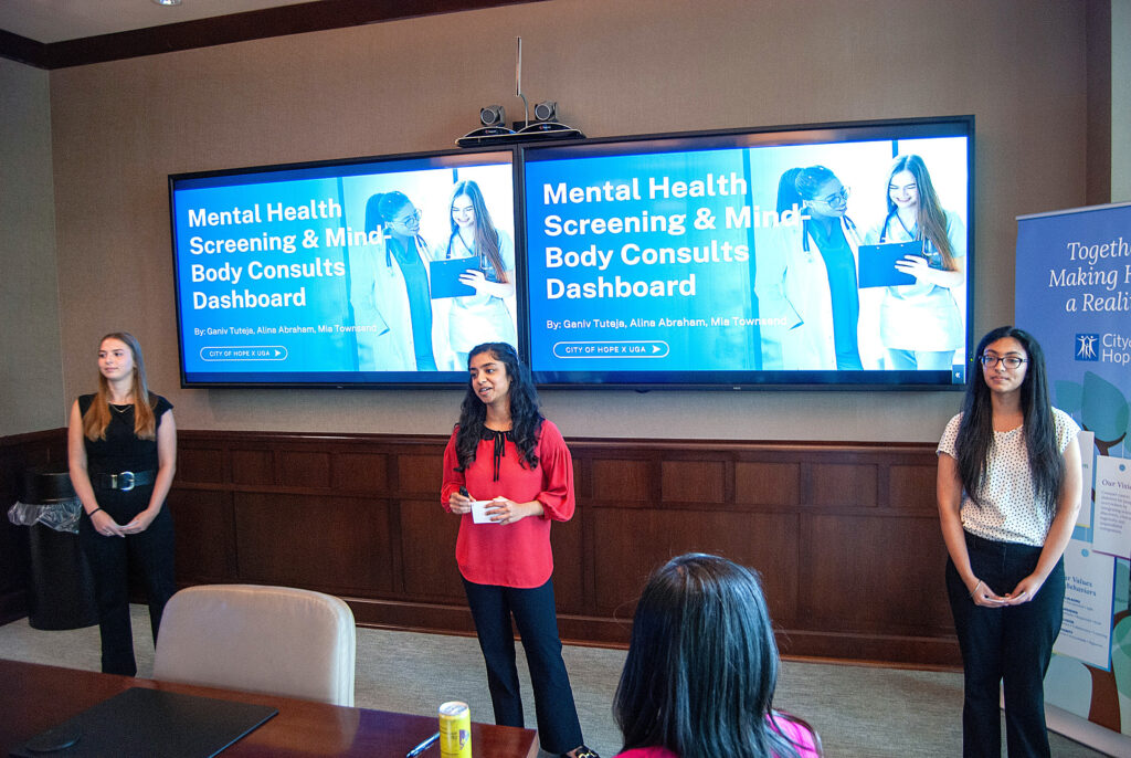 Three UGA students present in a board room in front of slides that read "Mental Health Screening and Mind-Body Consults Dashboards" data-driven health support