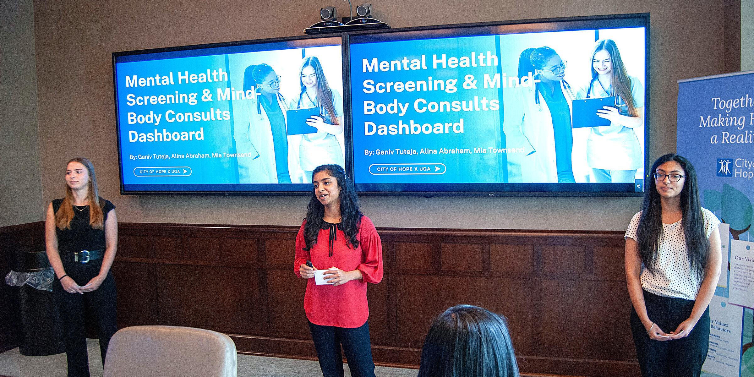 Three UGA students present in a board room in front of slides that read "Mental Health Screening and Mind-Body Consults Dashboards" data-driven health support