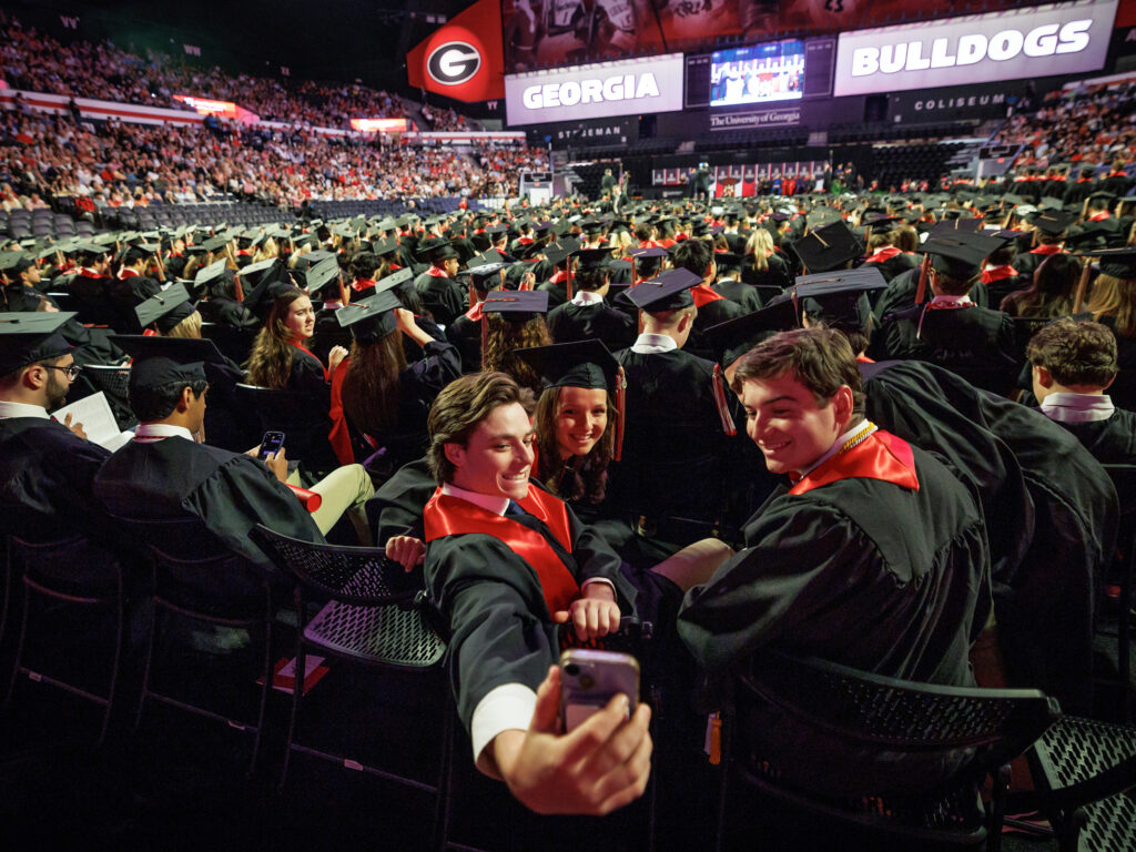 Two male and one female strudent take a selfie in Stegman Coliseum before 2025's undergraduate convocation.