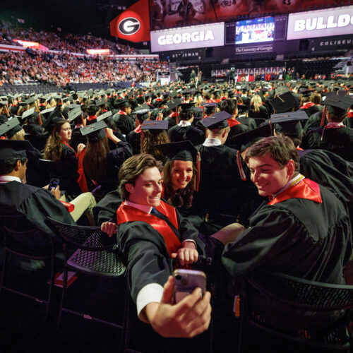 Two male and one female strudent take a selfie in Stegman Coliseum before 2025's undergraduate convocation.