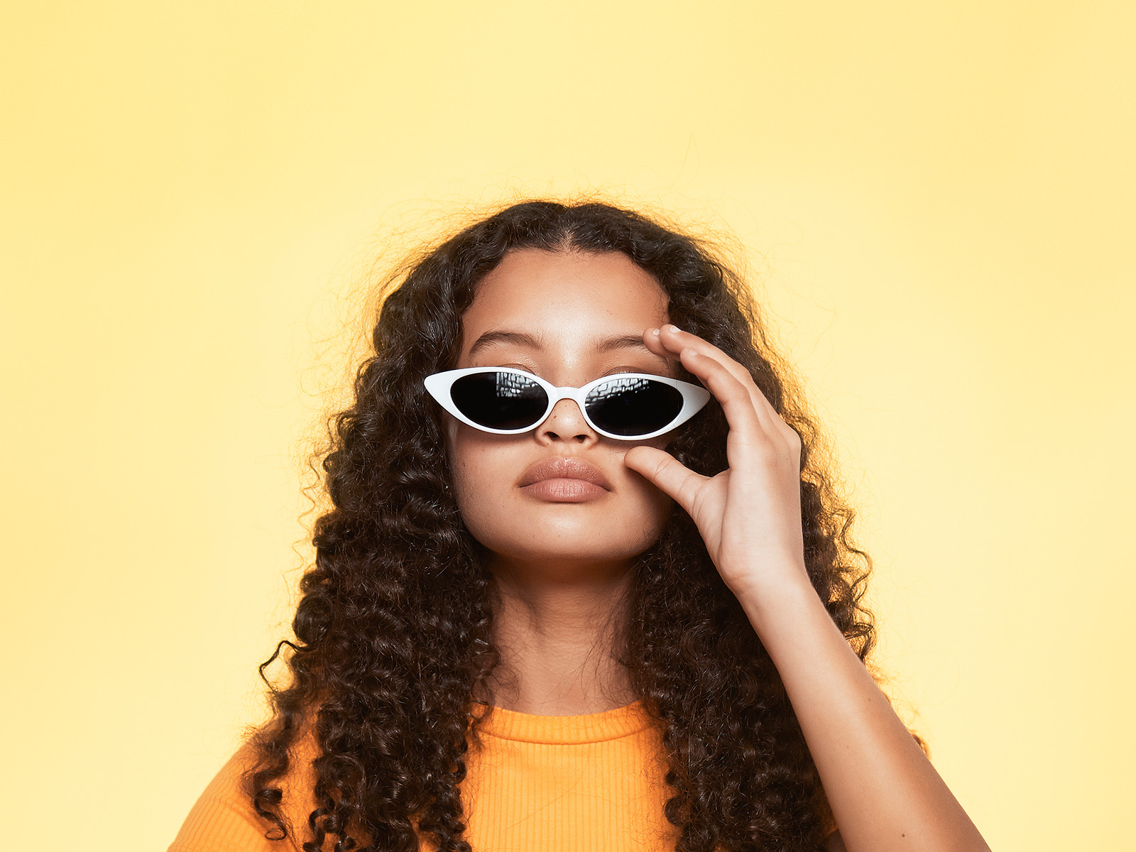 A woman with a cool stare adjusts her cat eye sunglasses.