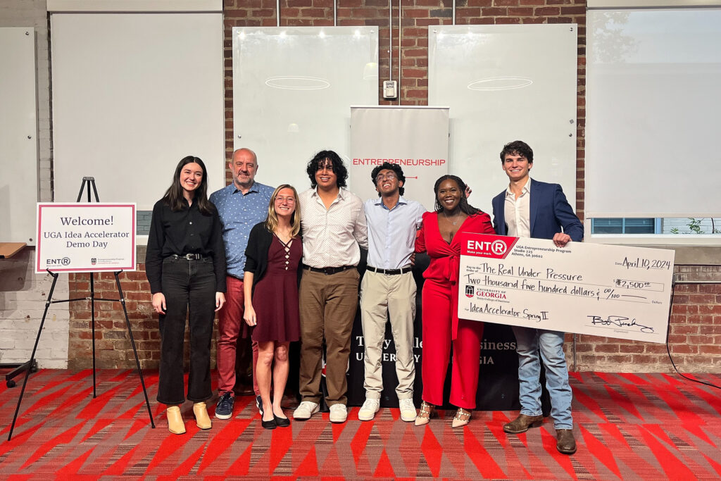 Judges and finalists at the 2024 Spring Idea Accelerator Demo Day gather on the Studio 225 Pitch Deck with the winner holding a large novelty check.