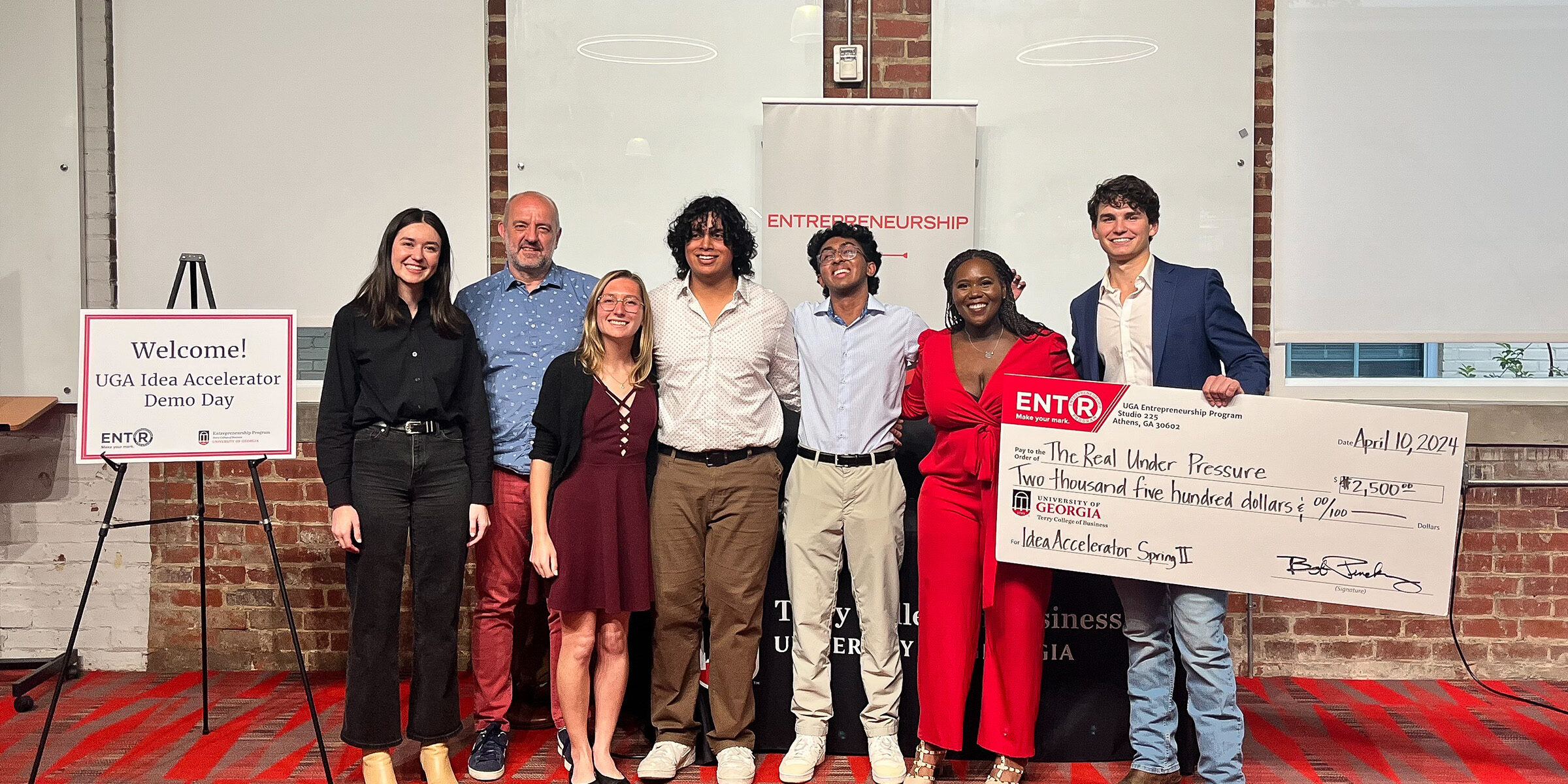 Judges and finalists at the 2024 Spring Idea Accelerator Demo Day gather on the Studio 225 Pitch Deck with the winner holding a large novelty check.